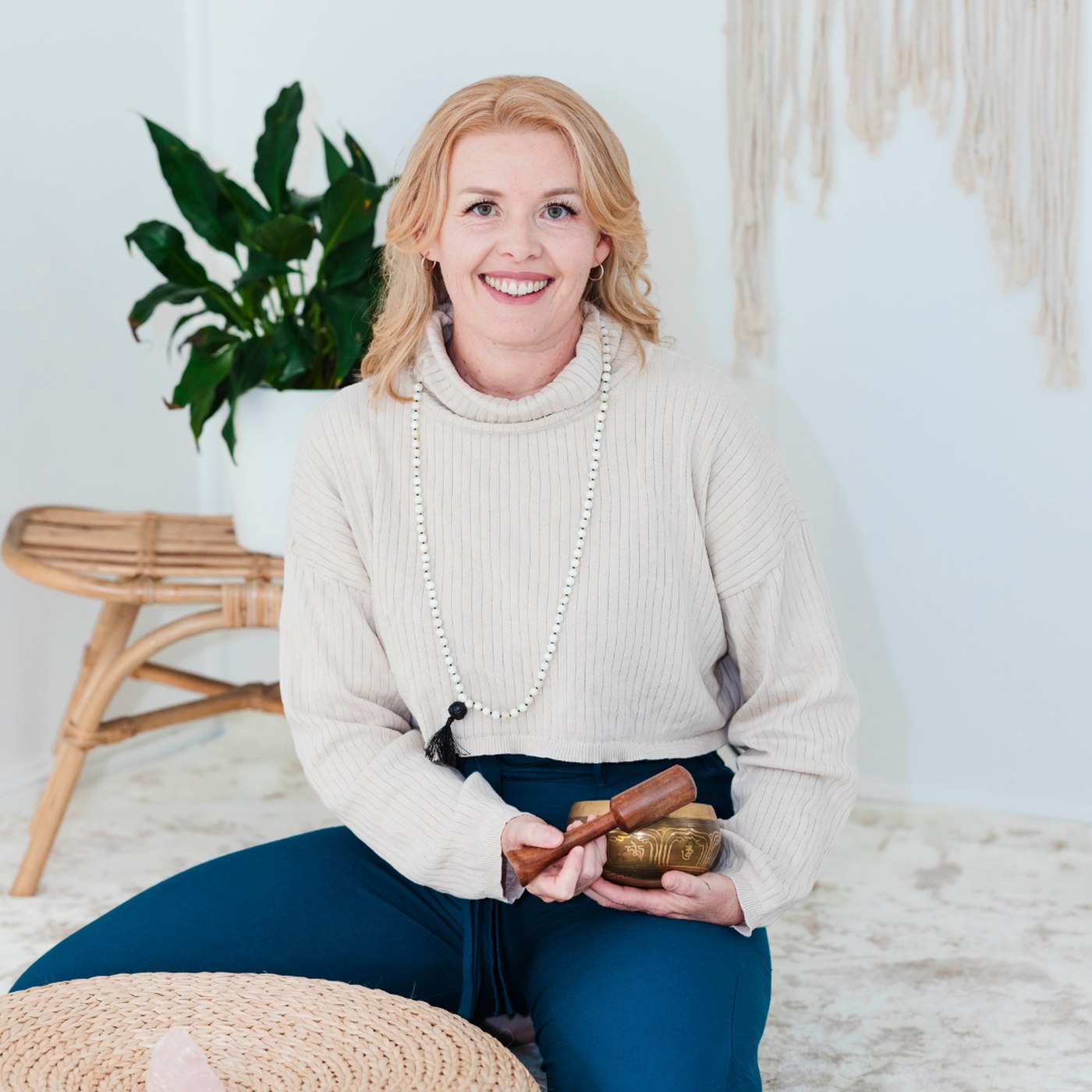 Fionna kneeling on a soft rug with a singing bowl, beside a woven floor cushion